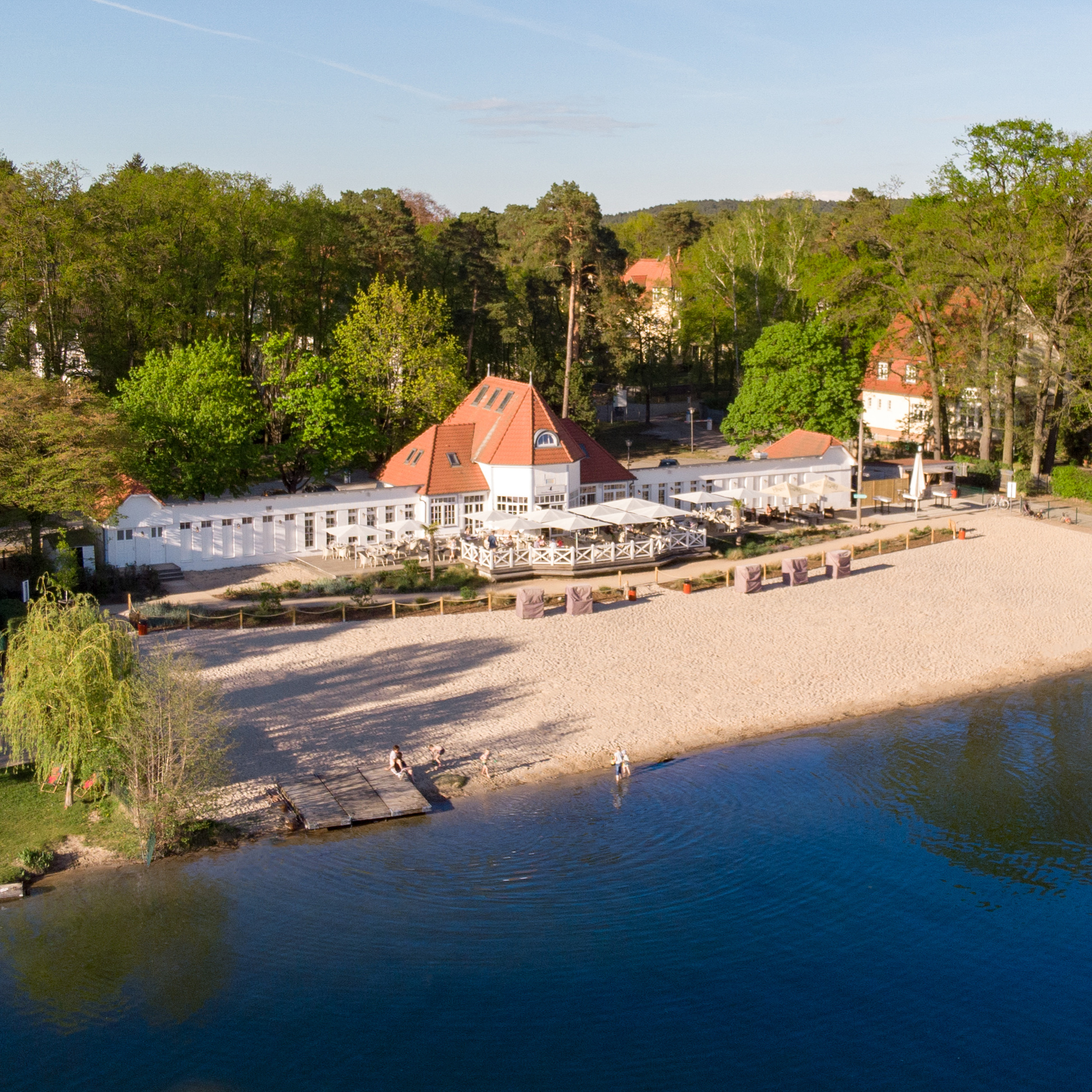 Urlaub am See: Drohnenaufnahme vom SeeBadSaarow, einem weißen Restaurant mit eigenem Strandabschnitt am Scharmützelsee - Hotel Esplanade Resort & Spa Bad Saarow
